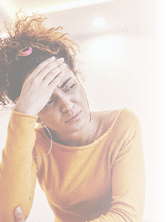 Attractive caucasian tanned brunette with curly hair sitting on sofa in living room,holding head and having headache 